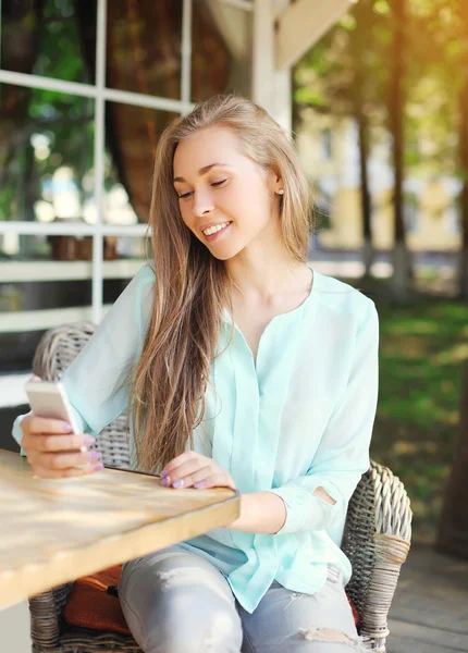 Счастливая симпатичная улыбчивая женщина пользуется смартфоном в кафе — стоковое фото