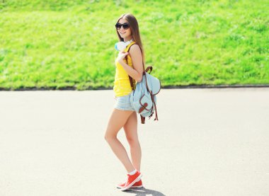 Güneş gözlüğü ve sırt çantasında bir kulaklık giyen mutlu güzel kız