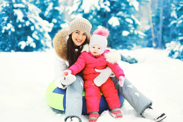 Happy mother and child sitting together on sled in winter snowy — Stock Photo, Image