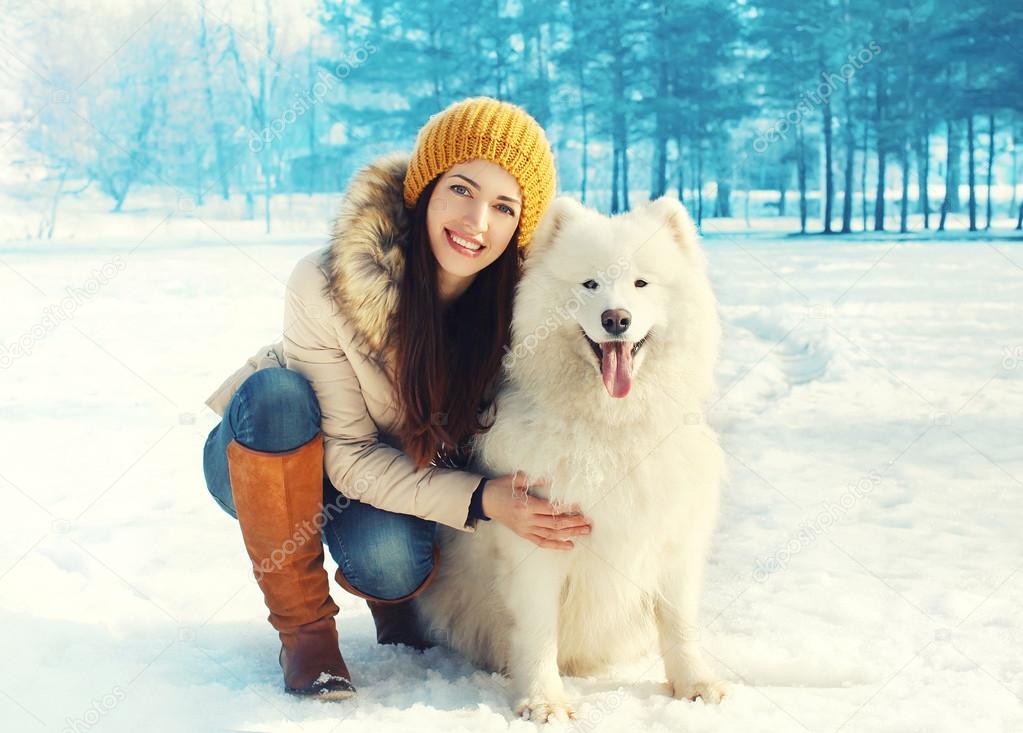 Happy smiling woman owner embracing white Samoyed dog in winter