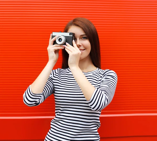 Ładna kobieta z retro starodawny aparat w mieście nad czerwonym backgrou — Zdjęcie stockowe
