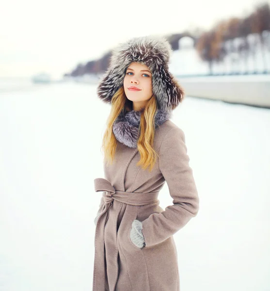 Hermosa mujer sonriente con un abrigo y un sombrero sobre la nieve en invierno —  Fotos de Stock