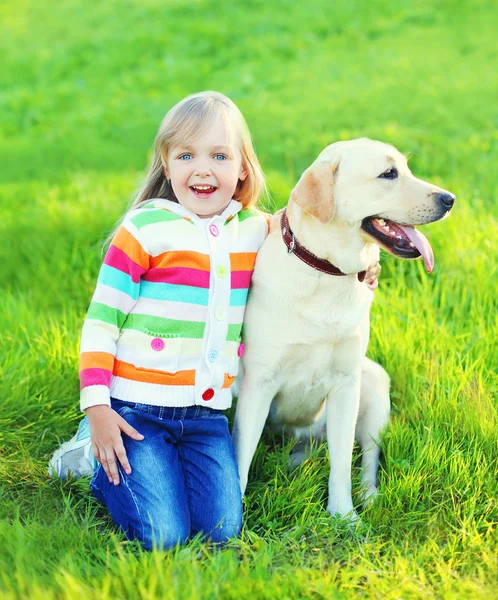 Gelukkig kind met labrador retriever hond op gras in de zomer — Stockfoto