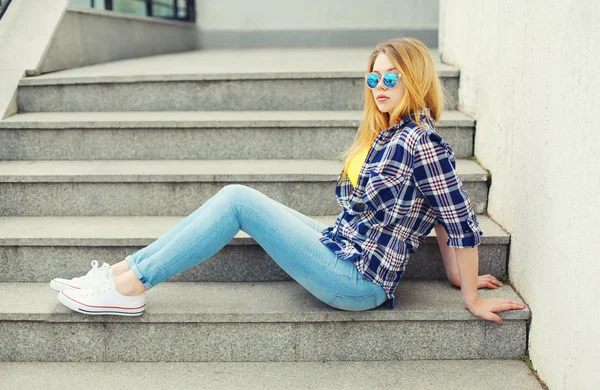 Pretty young girl wearing a checkered shirt and sunglasses sitti — Stock Photo, Image