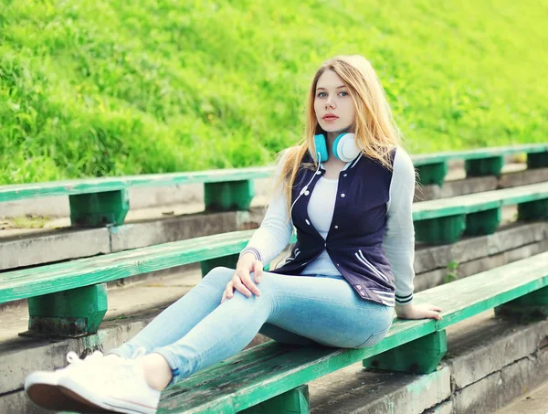 Chica joven con auriculares sentado escucha música en el parque de la ciudad —  Fotos de Stock