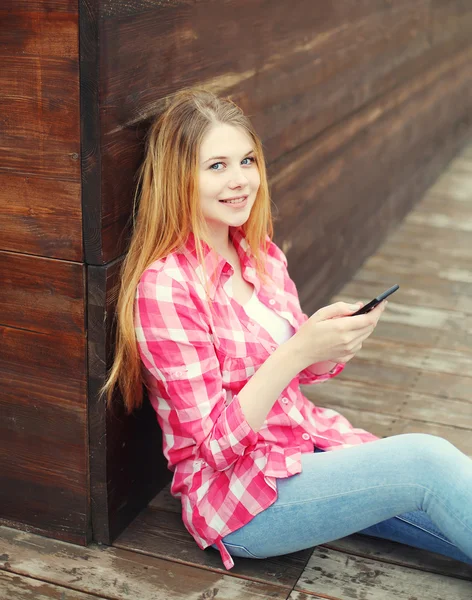 Молодая улыбающаяся девушка с помощью смартфона сидит в городе — стоковое фото