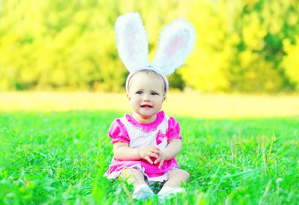 Happy cute baby with rabbit ears on grass in sunny summer day — Stock Photo, Image