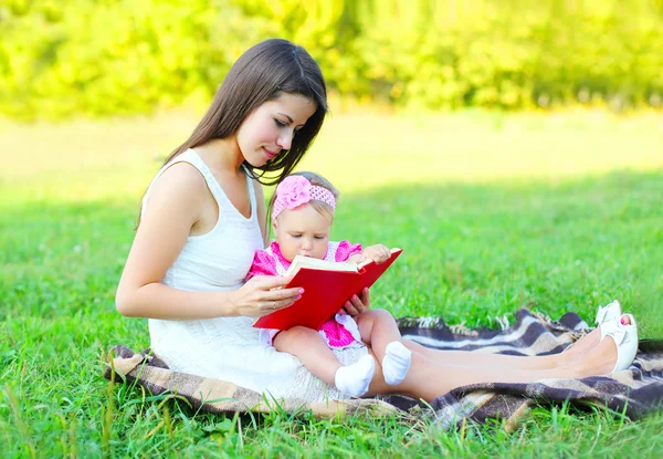 Madre feliz con el libro de lectura del bebé sentado en la hierba en verano d —  Fotos de Stock