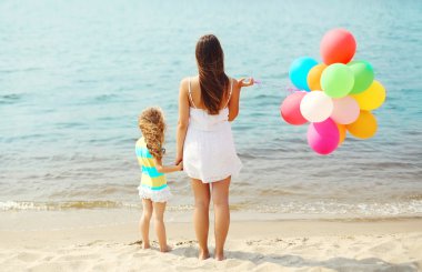 Anne ve çocuk s yakınındaki plajda durup renkli balonlar ile