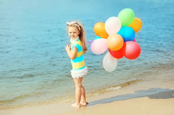 Happy child on summer beach with colorful balloons near sea — Stock Photo, Image