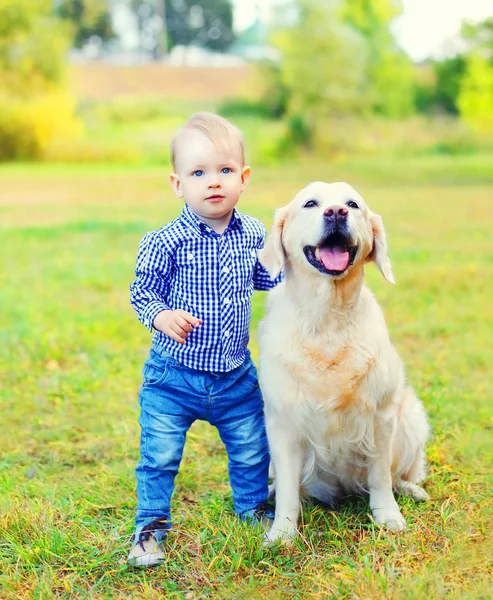 Weinig jongenskind en Golden Retriever hond op gras in park — Stockfoto