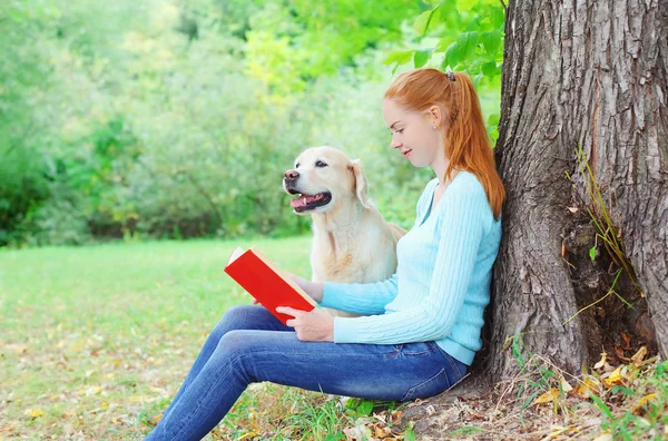 Счастливая хозяйка читает книгу с сидящей собакой золотого ретривера — стоковое фото