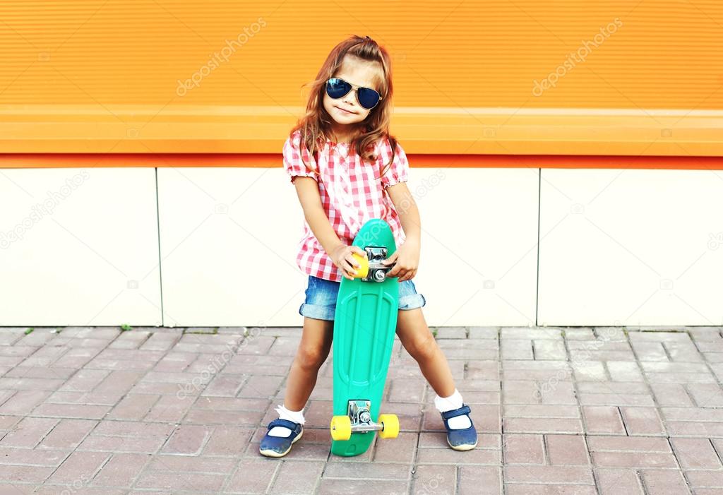 Fashion stylish little girl child with skateboard wearing a sung