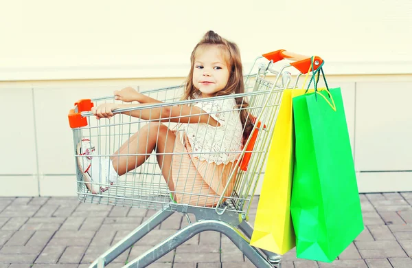 Gelukkig glimlachend kind zit in trolley trolley met kleurrijke shoppi — Stockfoto