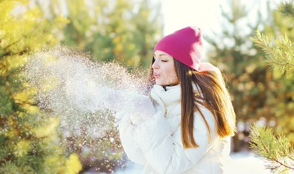 Glad ung kvinna blåser snö på händer i vinterdag — Stockfoto