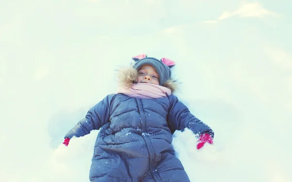 Lilla aktiva barnet liggande spelar på snö i vinterdag — Stockfoto