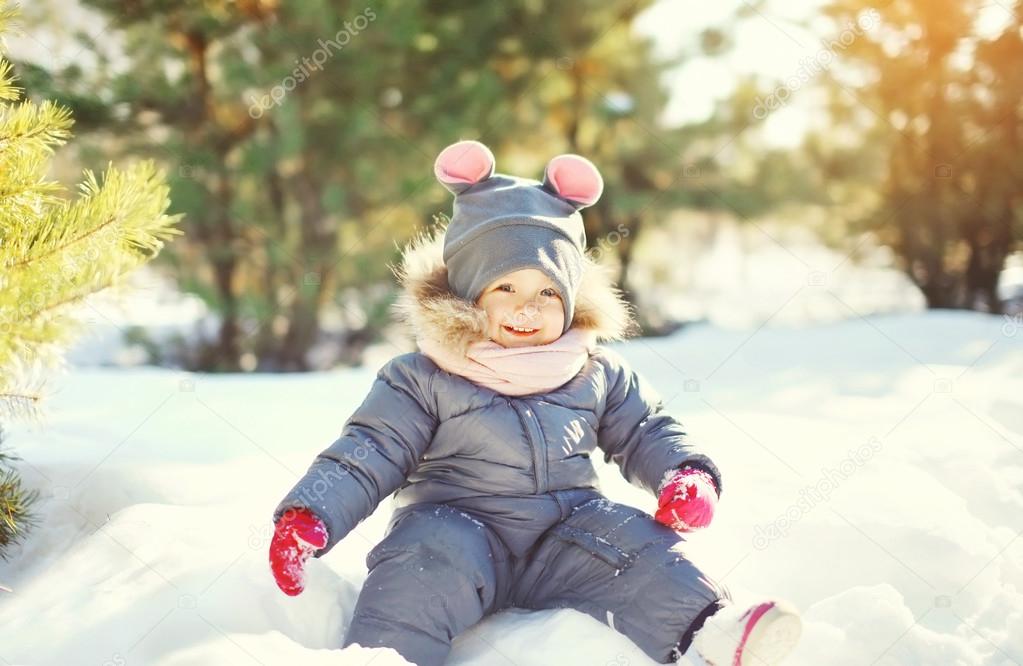 Cheerful smiling little child playing on snow in winter day
