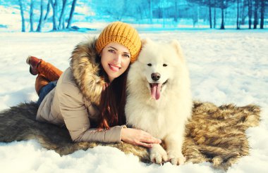 Mutlu gülümseyen kadın sahibi ve beyaz Samoyed köpek yatan kar
