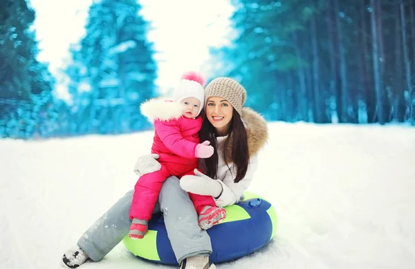 Gelukkig moeder en kind zittend op een slee in besneeuwde winterdag — Stockfoto