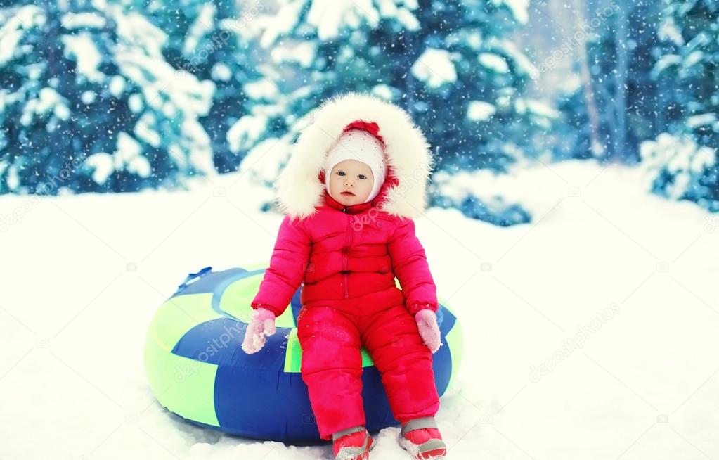 Little child sitting on sled in winter snowy day