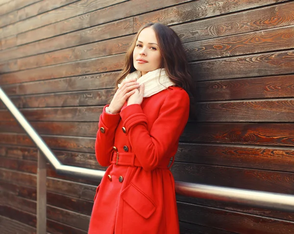 Beautiful young woman wearing a red coat in city over wooden bac — Stock Photo, Image