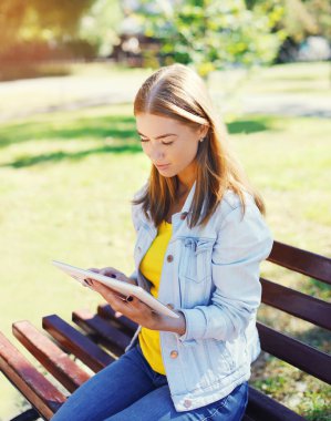 Beautiful young woman using tablet pc sitting on bench in city p
