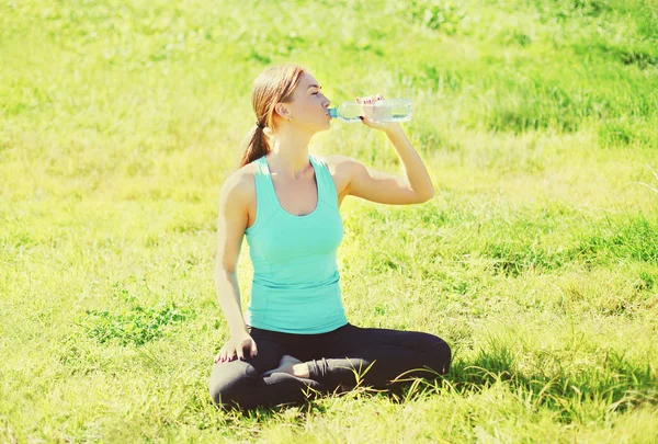 Sport, fitness, concept de yoga - femme assise sur l'herbe et drinki — Photo
