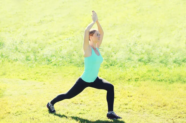 Young woman doing stretching exercises on grass in summer day — Stockfoto