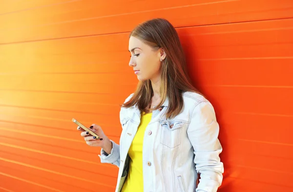 Красивая девушка с помощью смартфона в профиль над красочным оранжевым — стоковое фото