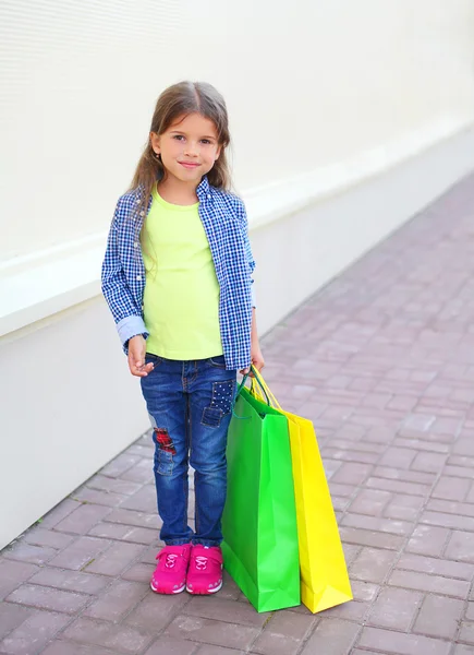 Hermosa niña pequeña con bolsas de papel de compras caminando en —  Fotos de Stock