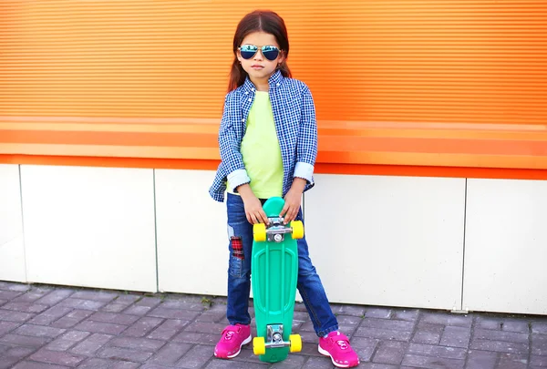 Elegante bambina con skateboard indossando un occhiali da sole a — Foto Stock