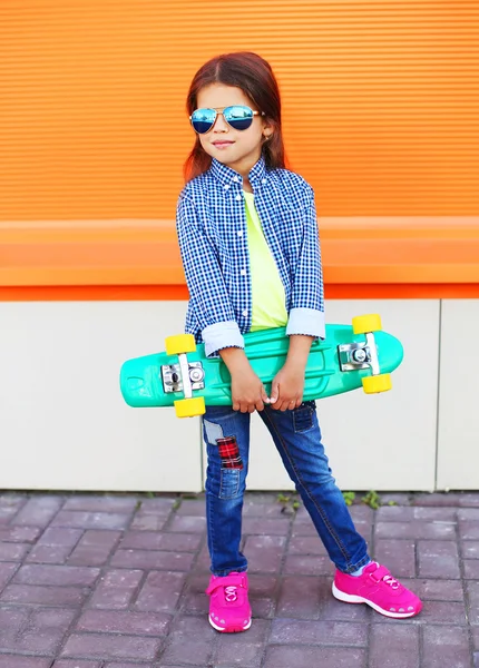 Stylish little girl child with skateboard over orange background — 图库照片