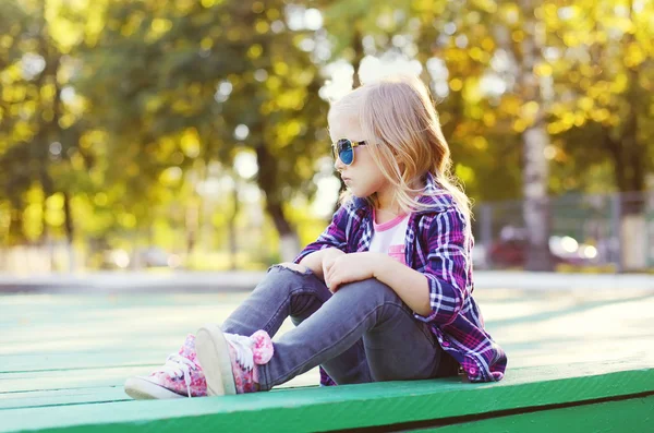 Child wearing a sunglasses and checkered shirt sitting in city p — Stock Photo, Image