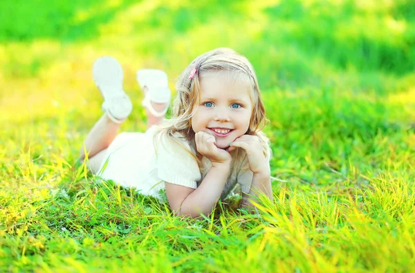 Güneşli Özetle çim üzerinde yalan mutlu sevimli gülümseyen küçük kız çocuğu — Stok fotoğraf