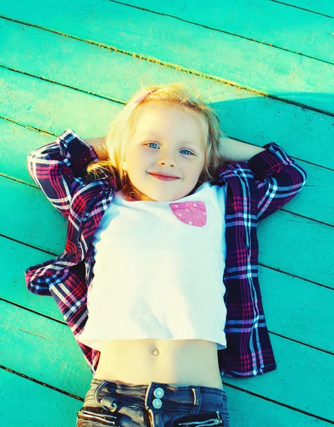 Щаслива маленька дівчинка дитина відпочиває на дерев'яній підлозі, руки позаду — стокове фото