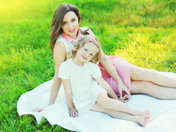 Gelukkig moeder en kind dochter samen op gras in zomerdag — Stockfoto