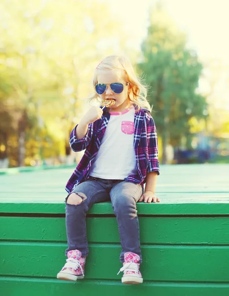 Liten flicka sitter med söt slickepinne i stadsparken — Stockfoto