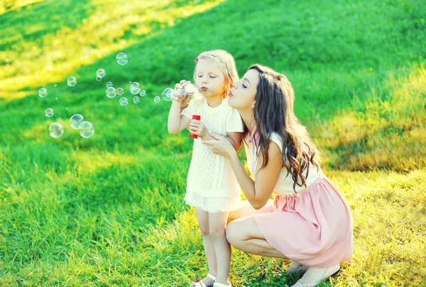 Мати з дитиною дме мильні бульбашки разом на траві в сумі — стокове фото