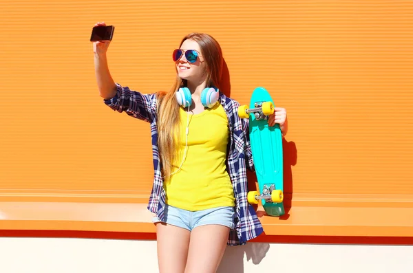 Chica sonriente bastante cool en gafas de sol con monopatín tomando pi — Foto de Stock