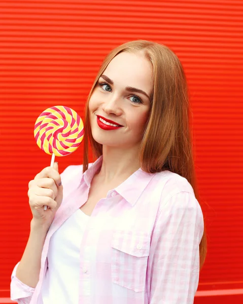 Retrato chica sonriente con dulce piruleta de caramelo sobre respaldo rojo — Foto de Stock