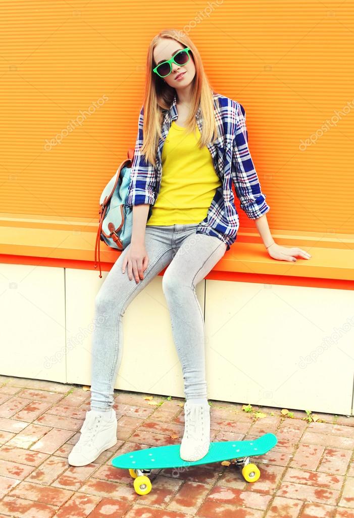 Fashion pretty girl with skateboard over colorful orange backgro