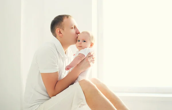 Glücklicher junger Vater küsst Baby zu Hause in weißem Zimmer in der Nähe von windo — Stockfoto