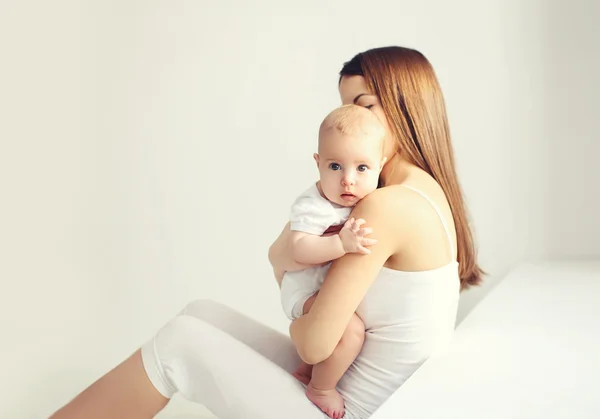 Madre con el bebé sentado en casa en habitación blanca cerca de la ventana —  Fotos de Stock