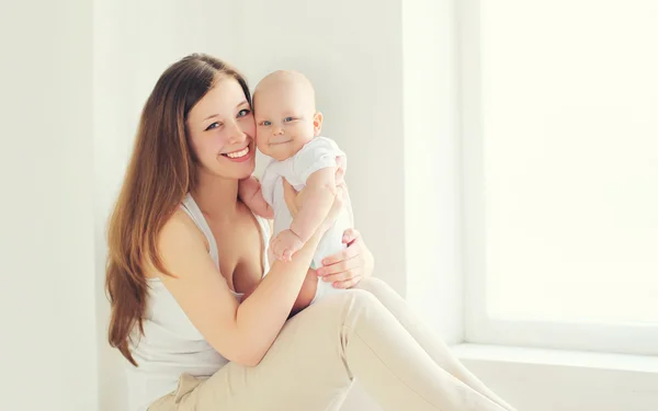 Mãe sorridente feliz com bebê em casa na sala branca — Fotografia de Stock
