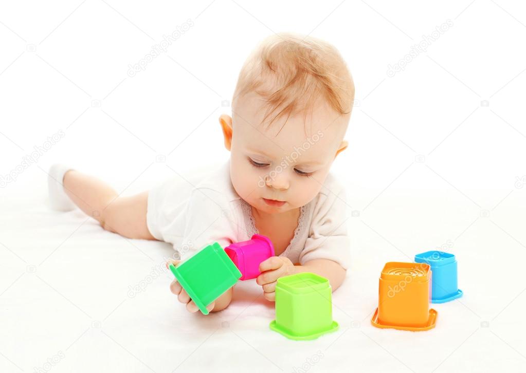 Baby lying playing with colorful toys on white background