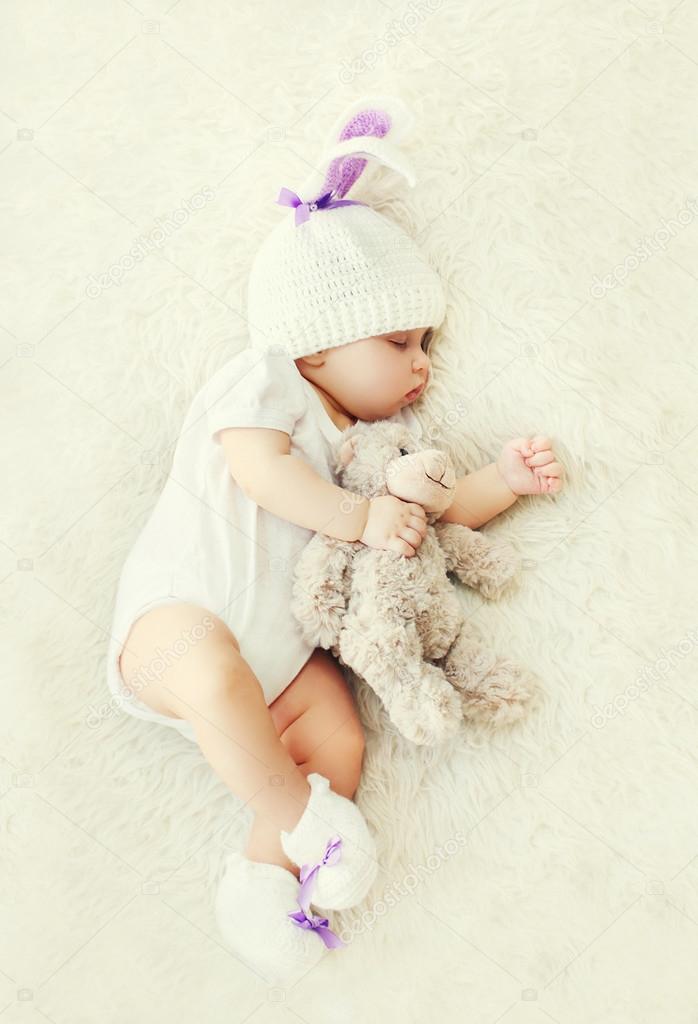 Sweet baby sleeping with teddy bear toy on white soft bed at hom