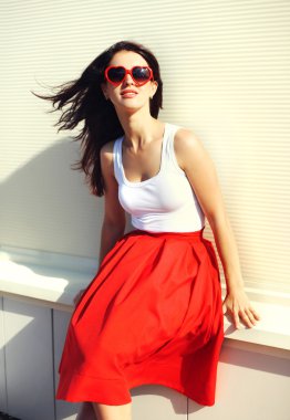 Güzel esmer kadın kırmızı güneş gözlüğü takıyor ve şehirde etek