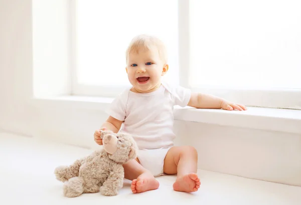 Baby with teddy bear toy sitting at home in white room near wind — Stock Photo, Image