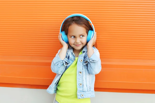 Happy child enjoys listens to music in headphones over orange ba — Stock Photo, Image