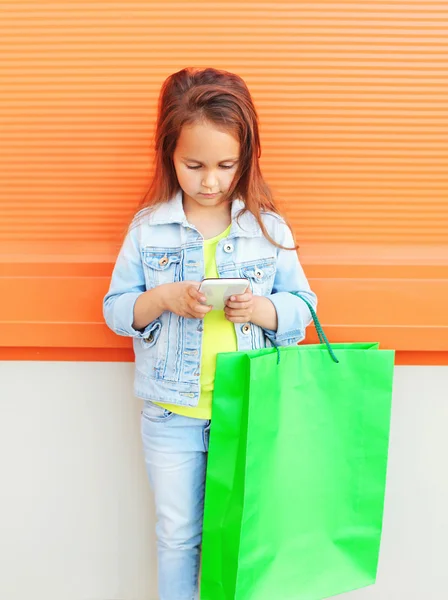 Criança menina com sacos de compras usando smartphone na cidade — Fotografia de Stock